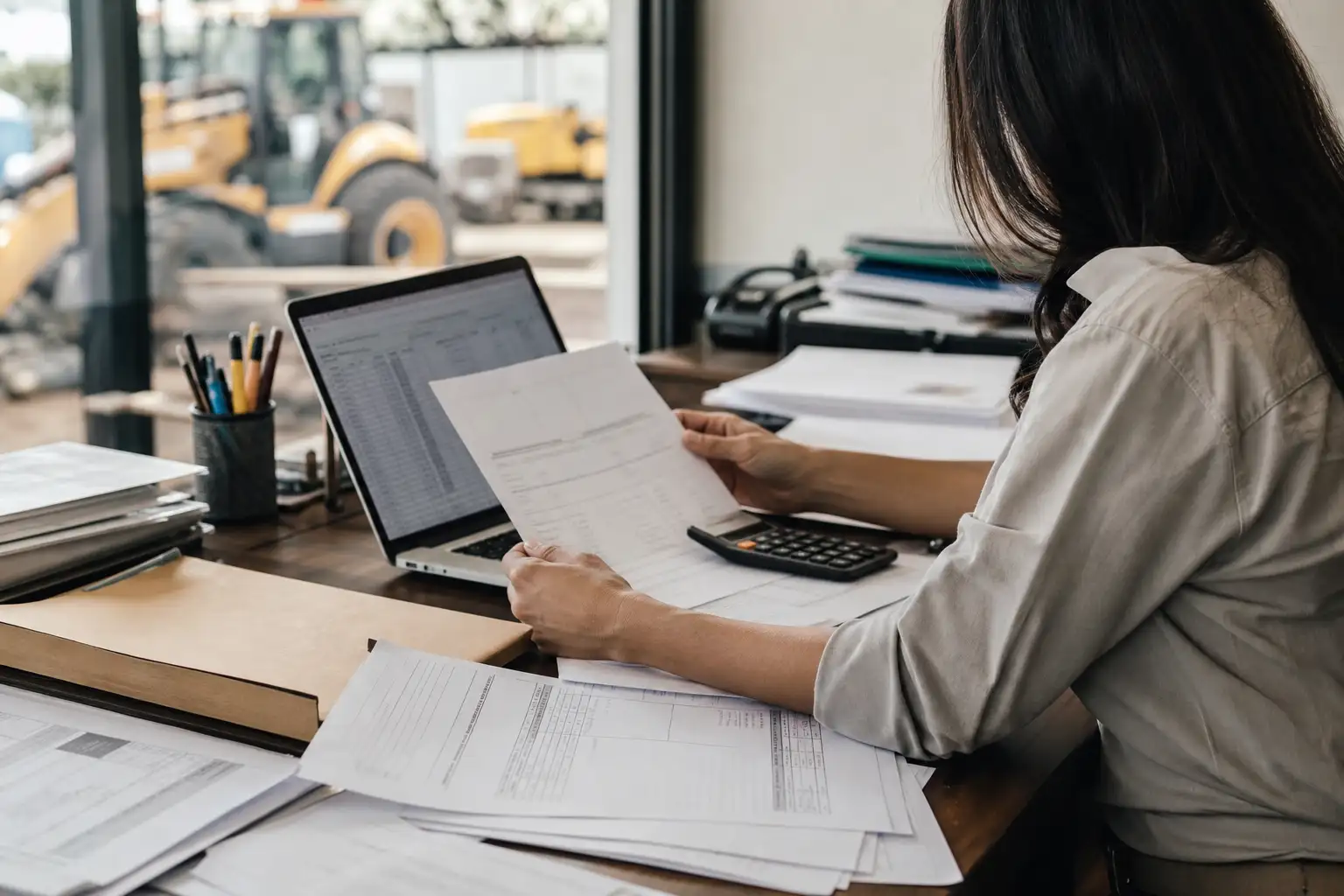 A finance or AP worker reviewing rental invoices, credit memos, and a spreadsheet at a desk in an office
