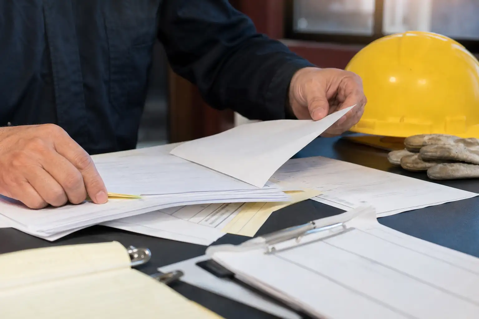 A finance or project office desk with a rental invoice, contract pages, a return ticket, and a clipboard beside a hard hat