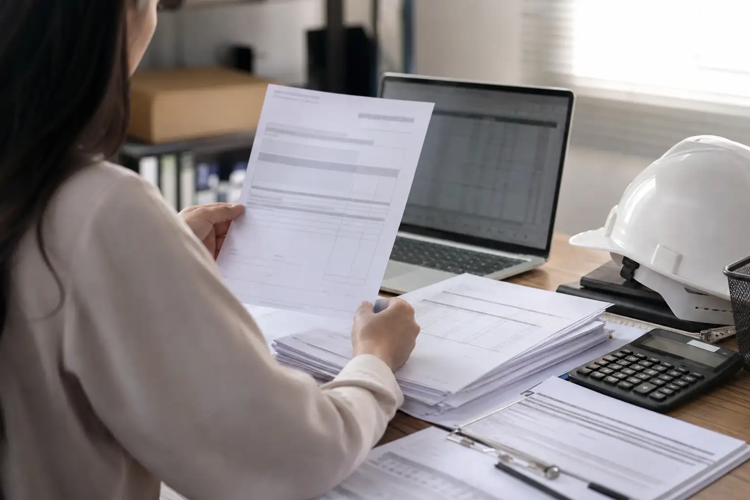An AP analyst reviewing rental invoices, a rate sheet, and a jobsite receipt at a desk