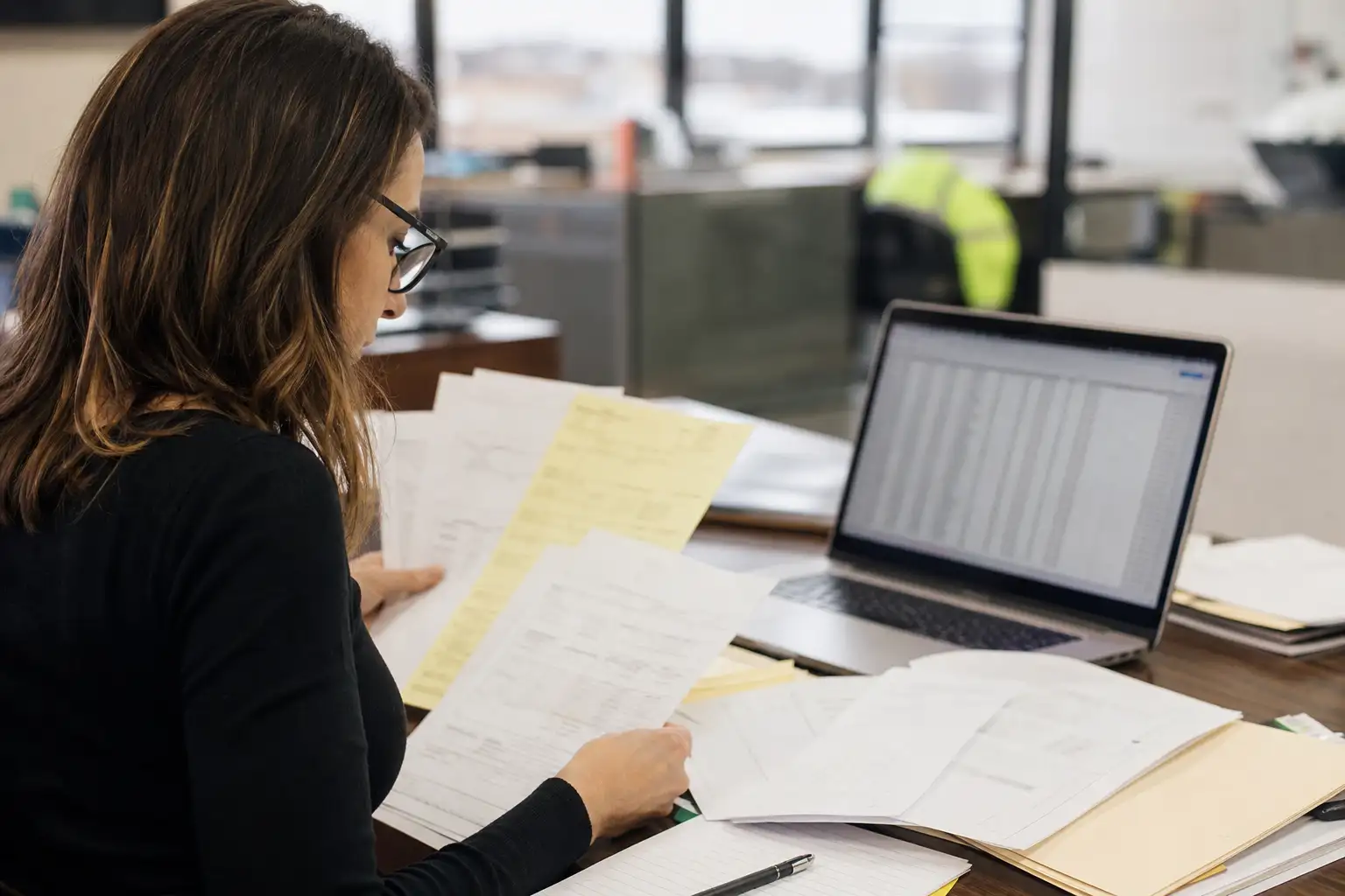An AP professional reviewing rental invoices and supporting paperwork at a desk with equipment rental documents spread out