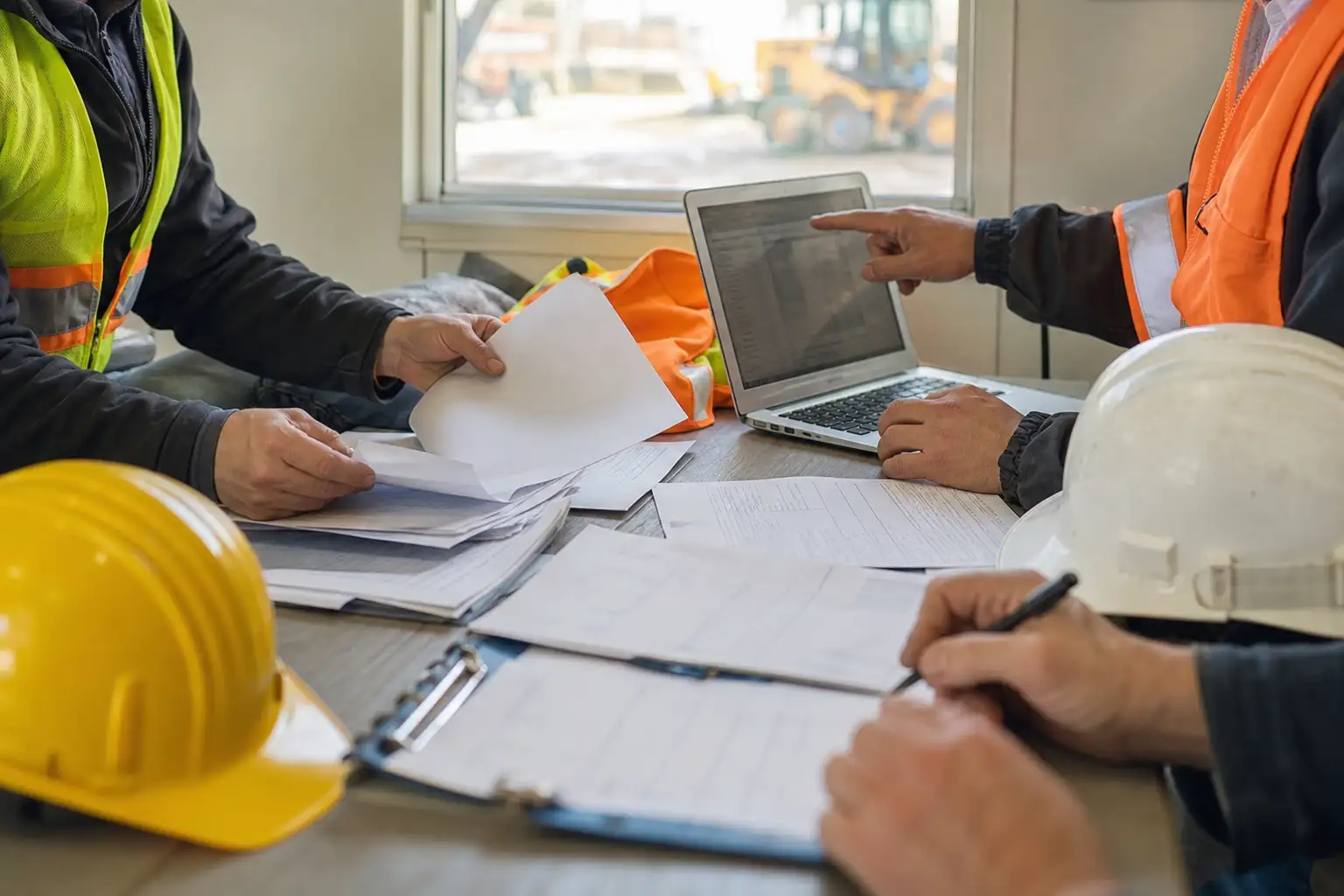 A finance and operations team reviewing rental invoices, off-rent tickets, and a laptop at a jobsite trailer table.