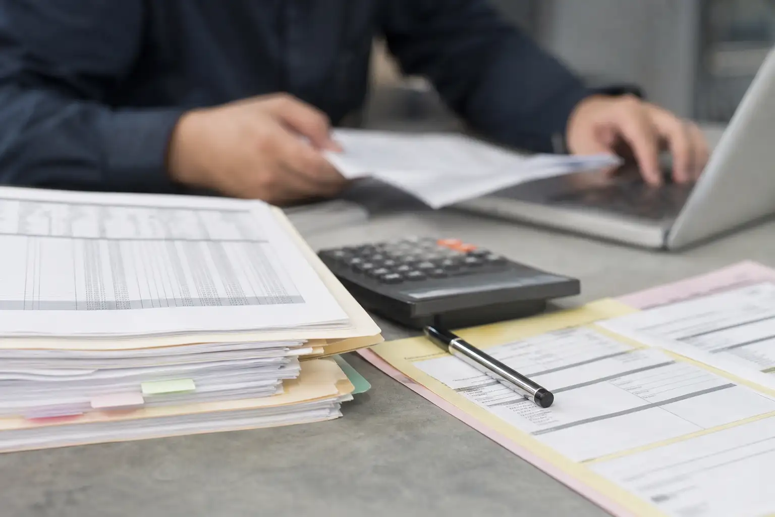 An office desk with a rental invoice, job files, and a calculator beside a laptop
