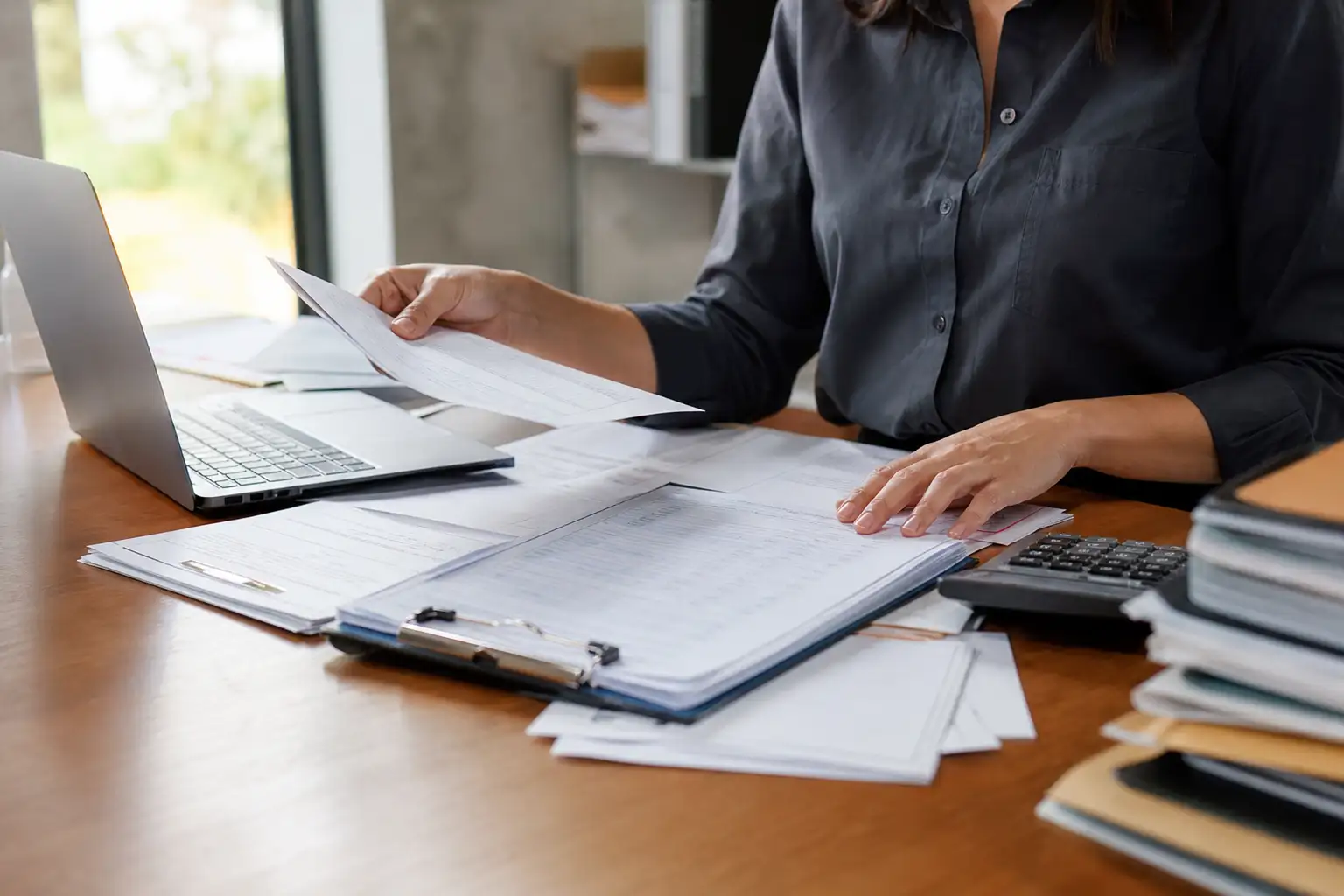 An office worker reviewing rental invoices, purchase orders, and a return log at a desk with a calculator and laptop.