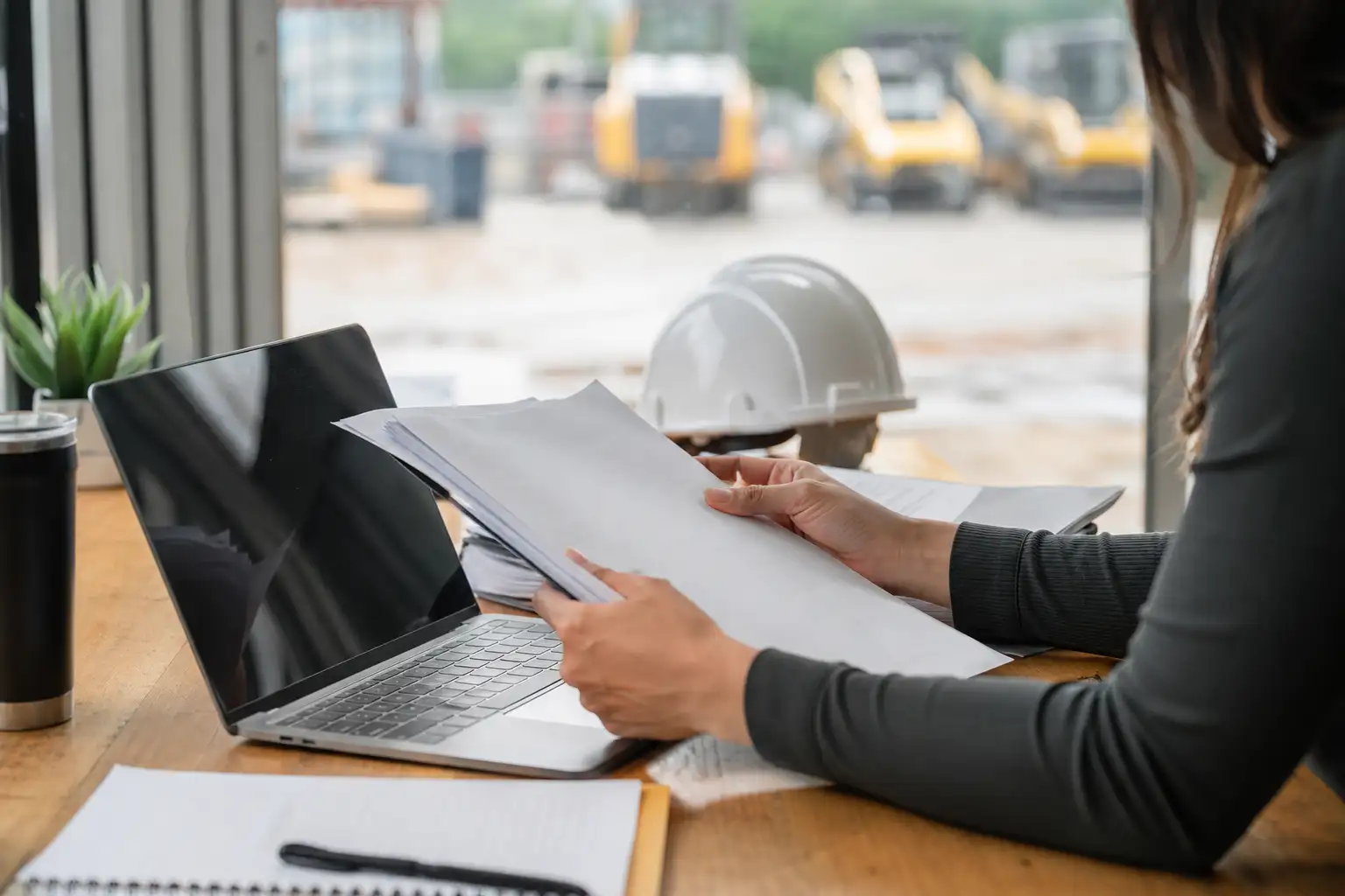 An office worker reviewing a rental invoice packet beside equipment rental paperwork and a laptop in a contractor accounting office.