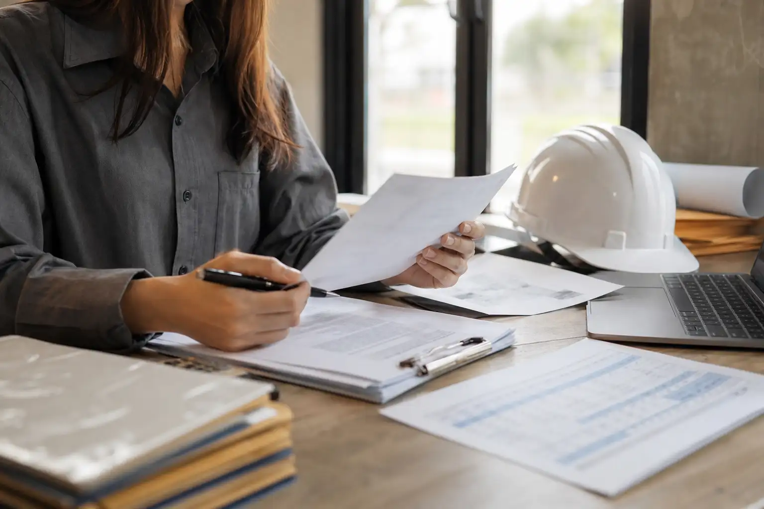 A finance or AP employee reviewing equipment-rental invoices, a contract packet, and a rate sheet at a desk